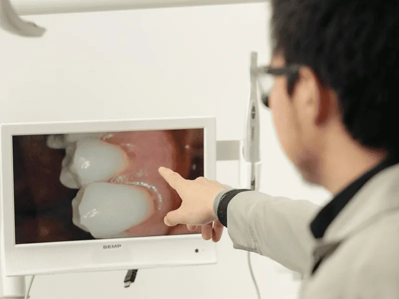 Dentista apontando para o monitor de uma câmera intraoral que mostra dois dentes ampliados